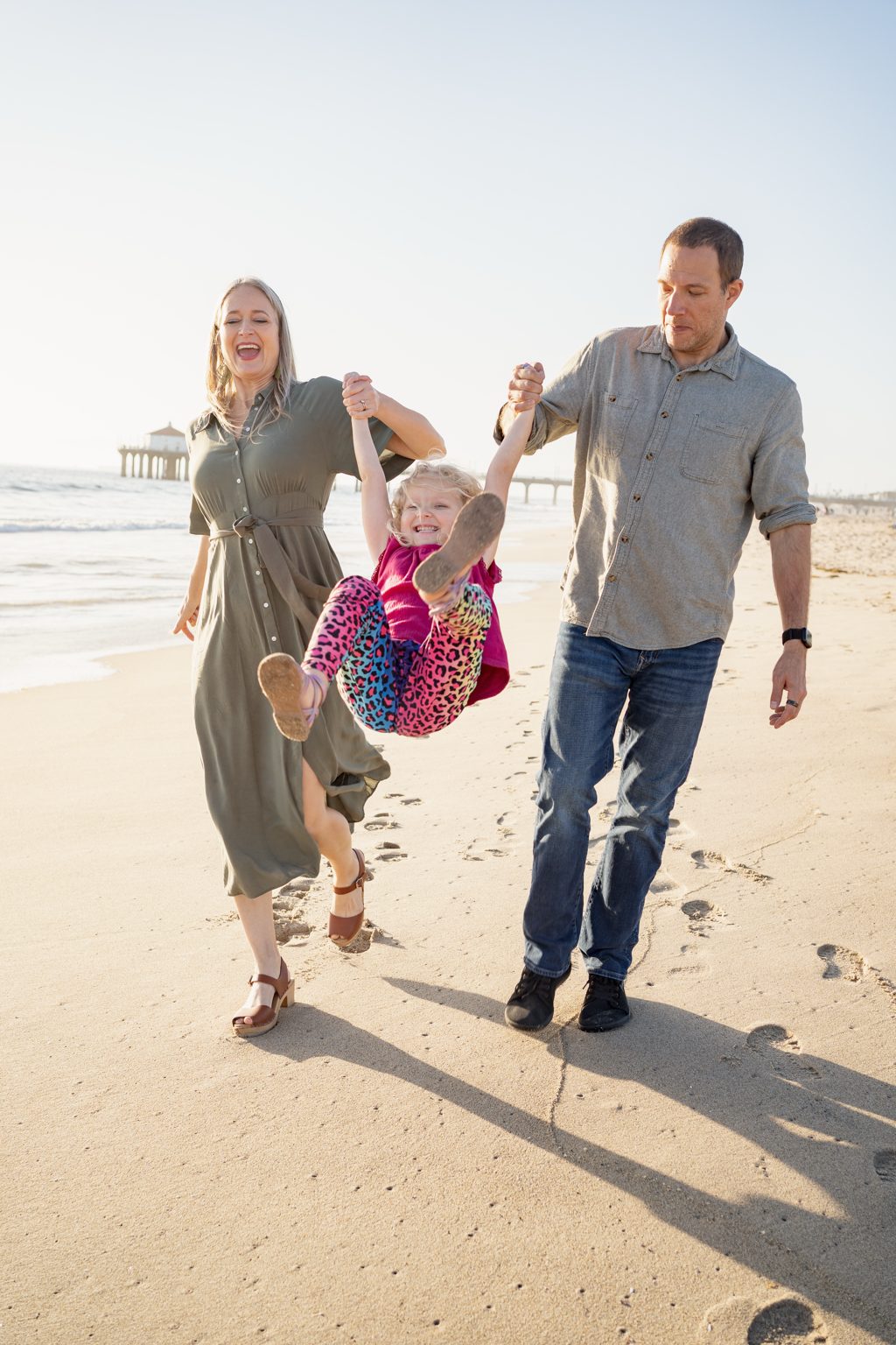 A mother and father swinging their laughing child between them on a sunlit beach